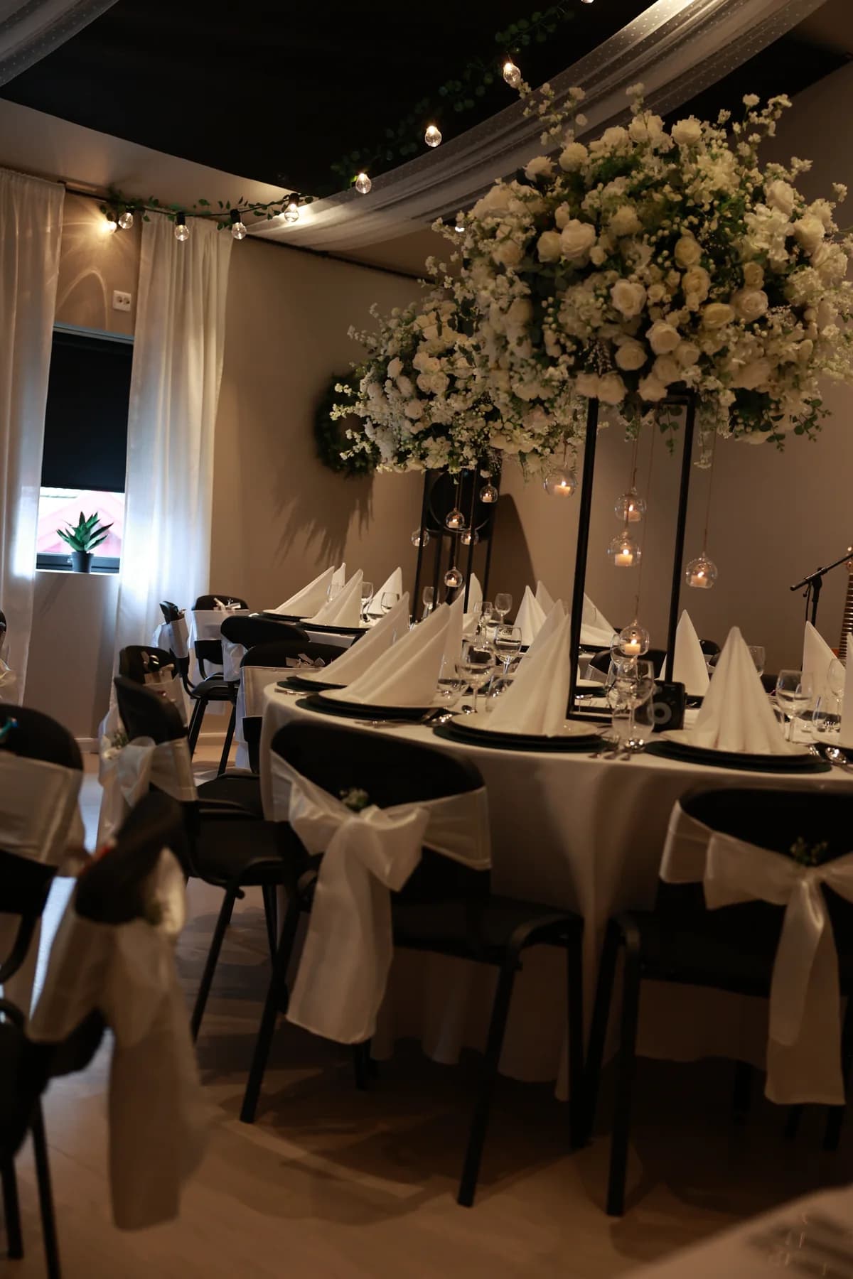Selskapslokalet dekket med runde bord og hvite blomster
